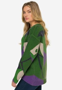 Maglione verde e accogliente con motivi astratti in viola e beige. Presenta un collo a giro e polsini a coste. Tessuto morbido, vestibilità rilassata.