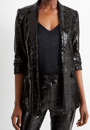 Sort paljet blazer og matchende bukser båret over en sort V-hals top, med blazer ærmerne rullet op til albuerne.