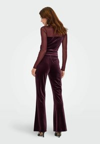 Bourgogne farvet velourdragt med lange mesh-ærmer, tætsiddende overdel, vide bukser og elastisk taljebånd. Glat tekstur og subtil glans.