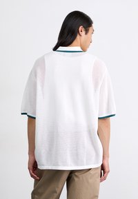 Hvit mesh polo skjorte med korte ermer, med grønn og hvit ribbestrikket krage og mansjetter, og en avslappet passform.