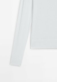 Pull en maille blanche à manches longues avec poignets et ourlet côtelés présenté sur un fond blanc uni.