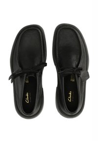 Scarpe in pelle nera con punte arrotondate, dettagli con lacci e superficie texture. Presentano un interno morbido e una suola in gomma. Marchio dorato visibile.