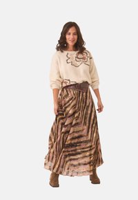 Suéter color marfil con bordado floral, combinado con una falda larga y fluida que presenta un patrón de rayas marrón y púrpura. Botines marrones completan el conjunto.