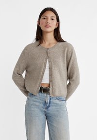 Light brown cardigan made of soft material, featuring a round neckline, front button closure, and long sleeves. Paired with high-waisted jeans.