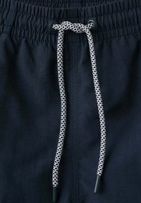 Ceinture en tissu noir avec élastique froncé et cordon à motif noir et blanc noué à travers deux œillets noirs.