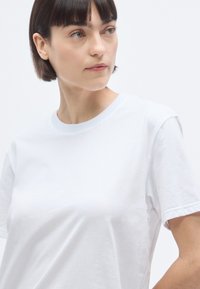 T-shirt en coton blanc avec un col rond, des manches courtes et une coupe décontractée. Texture lisse sans motifs ni logos visibles.