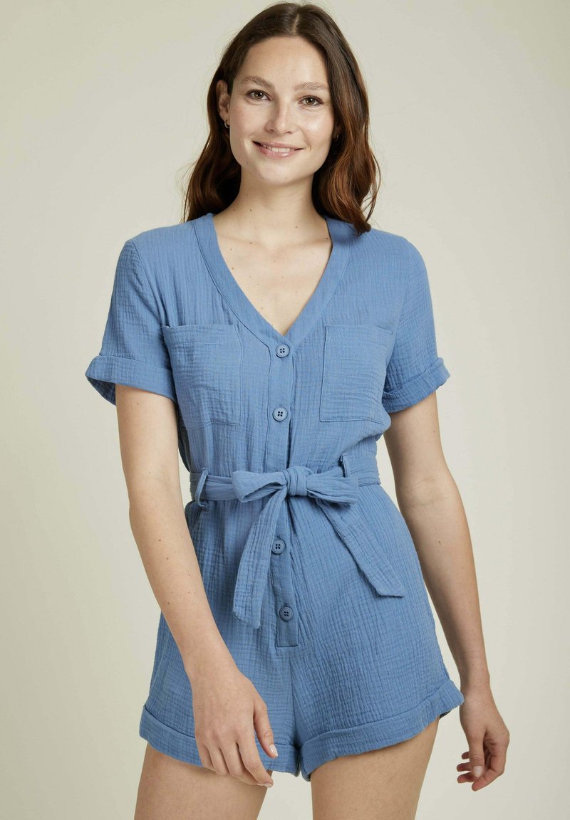 Romper en coton bleu à manches courtes, avec un devant à boutons, deux poches poitrine et une ceinture à nouer à la taille ; tissu texturé et manches retroussées.