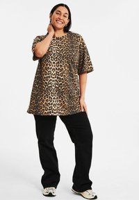 Fläckig leopardmönstrad topp med kort ärm i beige och svart, i kombination med svarta byxor och sneakers. Löst snitt med rund halsringning och mjukt tyg.