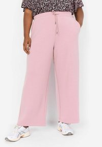 Ljust rosa vida sweatpants med dragsko i midjan, med sidofickor, mjuk textur, i kombination med vita sneakers.