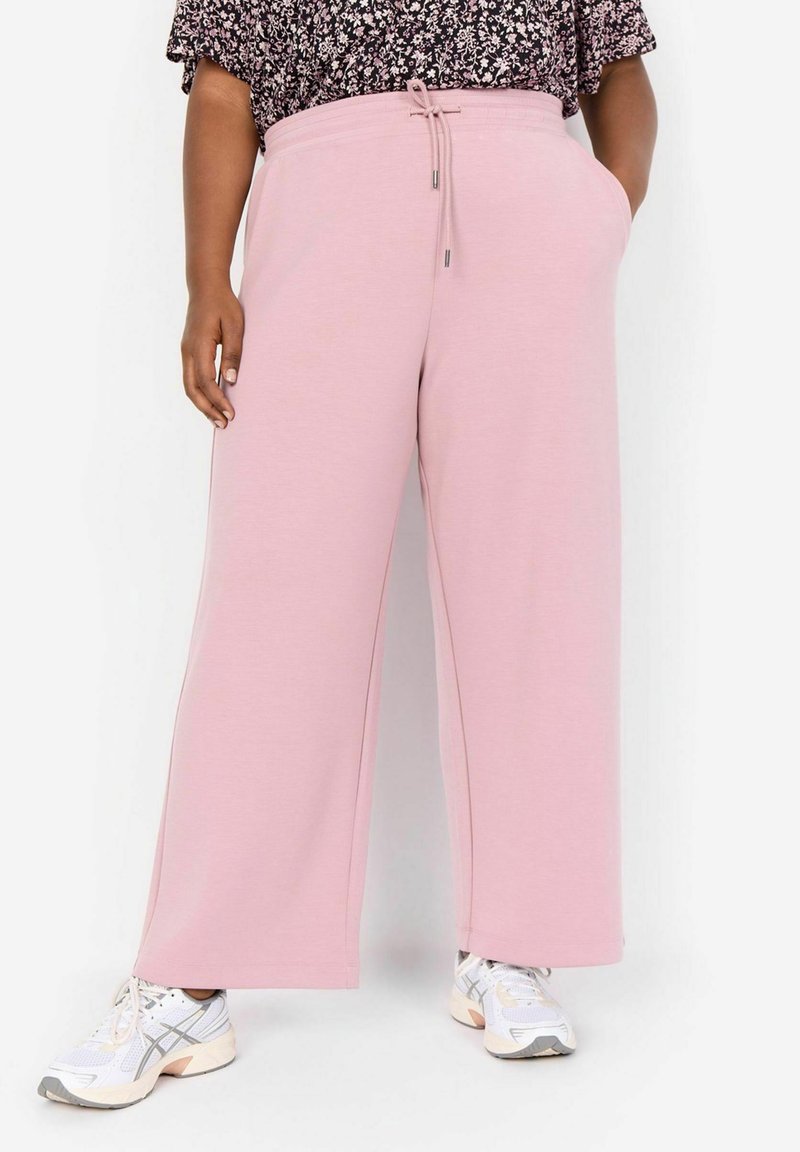 Ljust rosa vida sweatpants med dragsko i midjan, med sidofickor, mjuk textur, i kombination med vita sneakers.