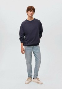 Sudadera navy con puños y cuello acanalados, combinada con jeans de color azul claro y zapatillas beige. Diseño simple y relajado sin patrones.