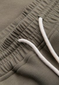 Gros plan sur une ceinture élastique grise avec cordon blanc sur un pantalon en tissu texturé.