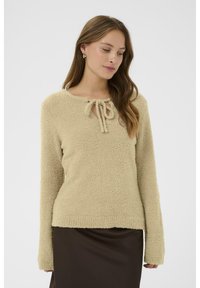 Beige, bolyhos pulóver hosszú ujjakkal, lekerekített nyakkal és elöl kötési részlettel. Az anyaga lágy és texturált.