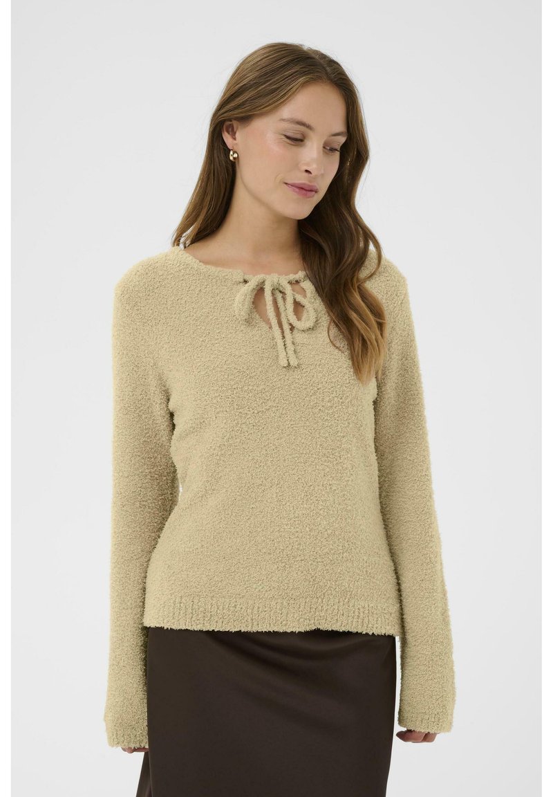 Beige, bolyhos pulóver hosszú ujjakkal, lekerekített nyakkal és elöl kötési részlettel. Az anyaga lágy és texturált.