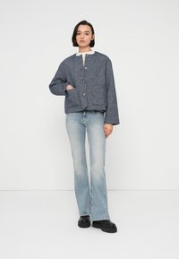 Γκρι σακάκι από μείγμα μαλλιού με στρογγυλεμένο γιακά, κουμπιά μπροστά και τσέπες με πάτο, συνδυασμένο με ανοιχτόγαλανες καμπανέ τζιν και μαύρα παπούτσια με πλατφόρμα.