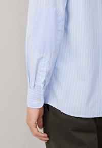 Camicia a maniche lunghe a righe blu con polsini con bottoni, caratterizzata da una toppa per il gomito di texture a contrasto e un taglio dritto all'orlo.