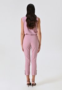 Top rosa senza maniche abbinato a pantaloni rosa aderenti con spacchi laterali all'orlo. Tessuto morbido e design su misura.