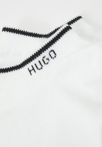 Witte sok met een zwarte streep aan de bovenkant; "HUGO" geborduurd in het zwart. Zachte textuur met ribstof voor een goede pasvorm en comfort.