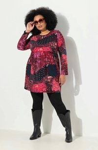 Färggklig långärmad klänning med ett blommigt och geometriskt mönster, utrustad med en nyckelhålskrage och två mörka fickor. Matchad med svarta leggings och stövlar.