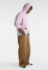 Sudadera con capucha de color púrpura claro con gráficos, superpuesta sobre una camisa de cuadros azul y blanca, combinada con pantalones de pierna ancha marrones y zapatos negros tipo slip-on.
