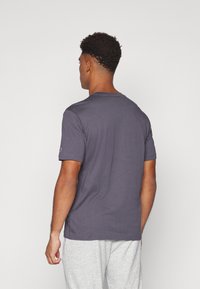 T-shirt en coton gris foncé à manches courtes et col rond. Présente un logo sur la manche gauche. Texture lisse, coupe décontractée.