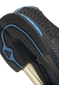 Lähikuva mustan ja sinisen Adidas-tennarien pohjasta, jossa näkyy kulutuspinta, pehmuste ja teksturoitu neulottu päällinen.