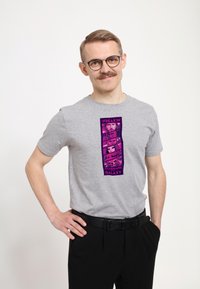 Grå bomullströja med en vertikal grafik i lila och svart, med bilder och text från "Guardians of the Galaxy". Korta ärmar, rundad halsringning.