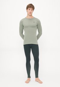 Langermet lys grønn topp med rund hals og logo, kombinert med mørkegrønne leggings med gradientmønster ved anklene.