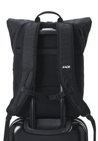 Schwarzer Rucksack mit gepolsterten, verstellbaren Trägern und Netzfutter, entworfen, um über Gepäckgriffen zu passen, mit einem oberen Traggriff.