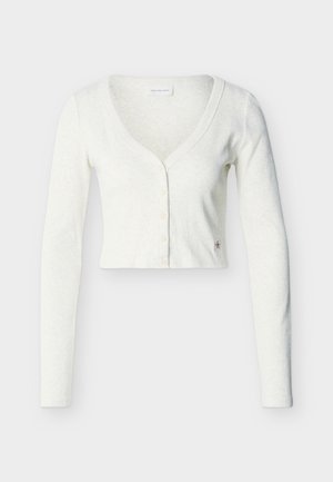 Valkoinen lyhyt neuletakki pitkällä hihalla, V-kaula-aukolla ja viidellä napilla edessä, yksinkertaisella vaalealla taustalla.