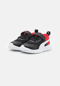 Chaussures de sport noires et rouges avec un upper en mesh, une sangle velcro et une semelle blanche. Comprend une languette pour un enfilage facile. Design texturé et léger.