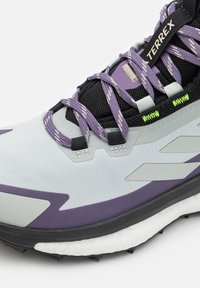 Scarpe da trail running Terrex in grigio chiaro e viola. Presentano una tomaia in mesh testurizzato, lacci flessibili e una suola nera resistente con chiodi.