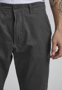 Grå bukser laget av lett stoff, med knappelukking, frontlommer og en jevn tekstur, med rett ben design.