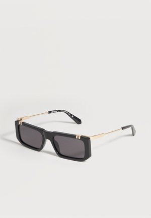 Lunettes de soleil rectangulaires noires avec montures épaisses et branches fines dorées, présentant des détails de marque sur les branches.