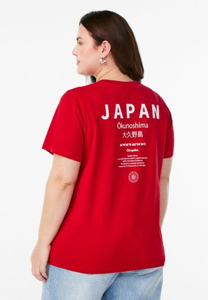 Červené bavlněné tričko s bílým nápisem "JAPAN" na zádech, obsahující text a grafické detaily o Ōkunoshimě. Uvolněný střih, kulatý výstřih.