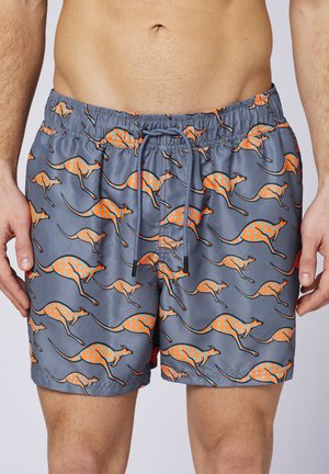 Man wearing gray swim shorts with orange kangaroo patterns and blue polka dots, elastic waistband, and drawstring.