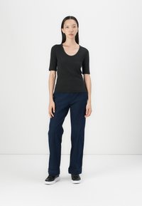 Zwarte korte mouwen top met een ronde hals, gecombineerd met losvallende donkerblauwe spijkerbroek met opvallende stiksels.