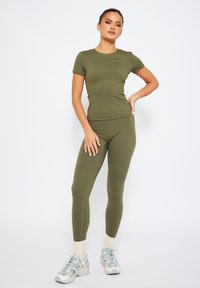 Olivgrön träningskläder i ett set som inkluderar en åtsittande t-shirt och leggings i mjukt, stretchigt material. Sneakers med en flerfärgad design fulländar looken.