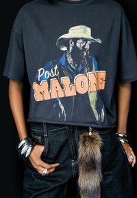 Black graphic T-shirt featuring a cowboy illustration with "Post Malone" text in large orange and white letters. Denim jeans with a faux fur keychain.