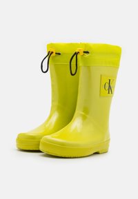 Botas de lluvia de goma amarillas con un acabado brillante, que cuentan con un cordón en la parte superior, detalles en negro y un parche de logo en el lado.