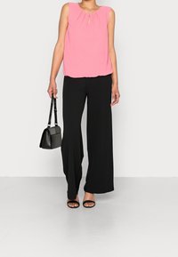 Růžová bezramínková blůza s klíčovou dírkou, zkombinovaná s širokými černými kalhotami. Černá kabelka a ploché sandály doplňují vzhled.