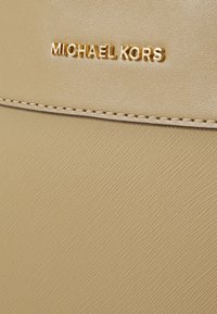 Sac Michael Kors en matériau texturé beige, avec un logo de marque en doré. Détail de couture lisse le long des bords.