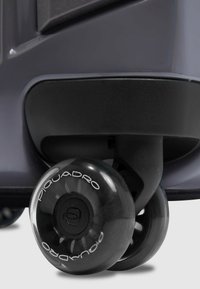 Schwarzes Kunststoff-Kofferrad mit transparentem Rand, auf dem der Markenname "Piquadro" zu sehen ist. Glatte Oberfläche mit abgerundeter Form.