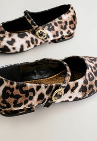 Chaussures Mary Jane à motif léopard avec un dessus en fausse fourrure noire, un petit talon bloc et un accent boucle en ton or. Design texturé et élégant.