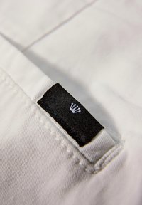 Étiquette en tissu noire avec un logo de couronne blanc cousu dans la couture d'un tissu en coton blanc, probablement une partie d'un vêtement.