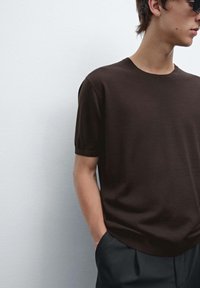 Hnědý pletený svetr s krátkým rukávem a kulatým výstřihem, lehký materiál a uvolněný střih, zkombinovaný s tmavými kalhotami.