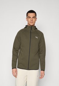 Veste zippée vert olive en tissu texturé, dotée d'une capuche, d'accents noirs et d'un logo Puma blanc sur la poitrine.