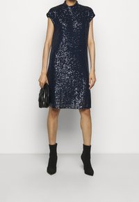 Navy sequin dress with a high collar and short sleeves, knee-length, paired with a black bag and black ankle boots. Smooth texture.