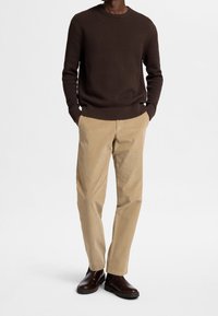 Suéter de punto texturizado marrón, pantalones de pana beige y botas de tobillo marrones oscuras. El conjunto incluye un cuello redondo y puños acanalados.
