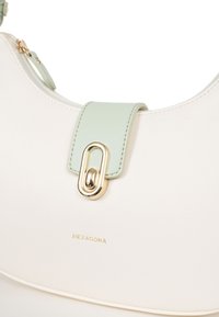 Witte leren handtas met een mintgroene accentriem en gouden hardware. Kenmerkt zich door een subtiele textuur en branding "HEXAGONA" in het goud.